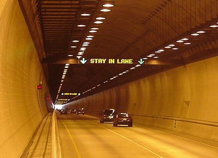 Traffic travels through the Cumberland Gap Tunnel, which connects TN and KY. An overhead sign in the tunnel displays the message "Stay in Lane."