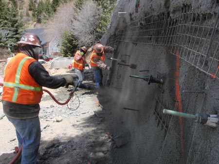 Figure 7. Photo. Three workers wearing safety vests and hard hats install soil nails during the construction of an earth retaining structure in Guanella Pass near Georgetown, Colorado. The soil nails were installed as part of a Federal Highway Administration Central Federal Lands Highway Division project.