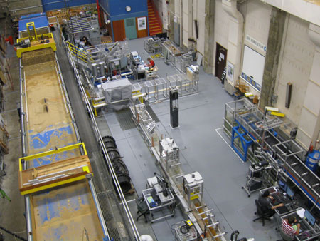 View from above of a very large, high-ceilinged room with many pieces of equipment, including a sedimentation flume elevated at the side of the room about midway between the floor and ceiling.