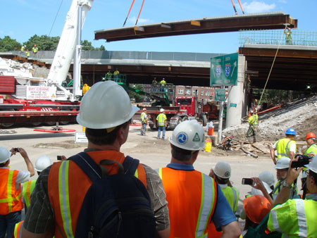 Participants in FHWA's Fast 14 project showcase observe work being done at the project site. Part of the bridge superstructure is being lifted by a crane.