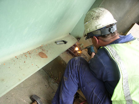 A close up of a worker repairing a bearing device on a bridge.