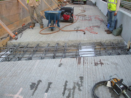 Workers prepare to close a bridge deck expansion joint. The uncovered joint is visible.