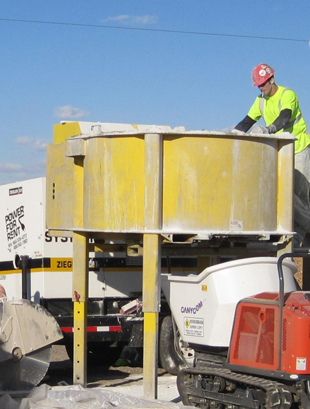 A worker uses a portable concrete pan mixer to prepare ultra-high performance concrete for placement during construction of field-cast connections. Additional construction equipment is in the foreground.