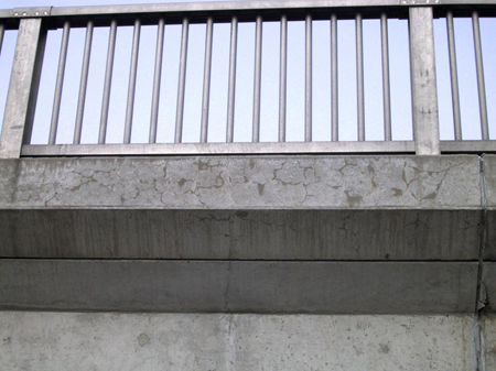 A close-up under-side view of a bridge railing. The edge beam supporting the railing has minor ASR-related cracking.