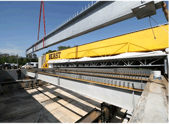 This photo shows a single-span bridge with large steel beams running across and over it. One of the beams is yellow and has the word "BEAST" in all caps on it.