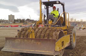 A pad foot roller compactor mounted with a blade is shown in an area of earth work.