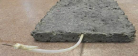 Photo of a lab sample (which looks like an asphalt pavement slab in a white wire coming out of it) of a bio-battery for a water quality sensor system.