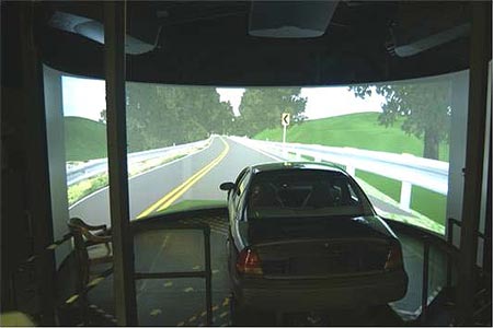 Photo of the Highway Driving Simulator at Turner-Fairbank Highway Research Center with an image of a two-lane road with guardrail on the screen Photo of the Highway Driving Simulator at Turner-Fairbank Highway Research Center with an image of a two-lane road with guardrail on the screen