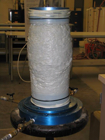 This photo shows a soil specimen used in triaxial tests. Compared to the specimen before testing, this specimen is shorter, bulges in the middle, and shows lumps at the surface.