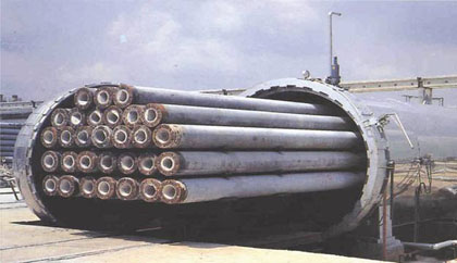 Photo. This photo shows a group of long concrete cylinder piles (hollow core) that are housed within a large tube canister.