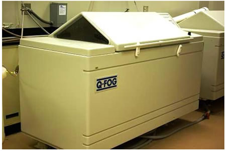 Figure 4. Photo. Salt-fog chamber. This photo shows a salt-fog chamber that consists of a unit to house the test panels while using cyclic corrosion of fog and dry-off processes. The unit is made of plastic and includes a custom controller to program the salt fog and drying cycles. A solution reservoir, which feeds salt solution for the fog cycles, is next to the housing unit. Test panels can be loaded into the chamber from the top by opening a pyramid shaped door. During the operation of the chamber, the door is secured using plastic hinges. The unit has the capacity to shut off by itself at the end of the test cycle. The fog chamber is installed on the floor and cannot be moved. 