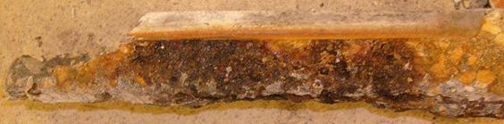 The plane of the crack is visible above the reinforcement. Along the plane, heavy orange-colored staining is observed.