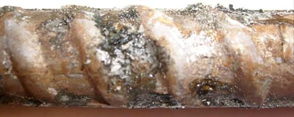 Galvanized reinforcement removed from concrete at crack initiation shows large regions covered by orange-brown corrosion products with isolated regions of intact zinc.