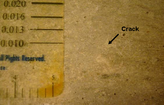 A faint white crack, less than 0.25 mm (0.01 inch) wide, is observed on the concrete surface.