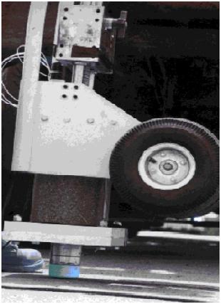 One-hundred-pound vibrator with dynamic load cell on bent 2. This image, taken at slightly above pavement level, shows a 100-pound vibrator with dynamic load cell on bent 2. The 100-pound vibrator was one of several sources of dynamic force tested to find a source that produced the frequency range of interest, which was 3 to 100 hertz.