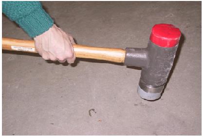 Twelve-pound impulse sledgehammer with soft gray rubber tip. This image shows the hand of a worker holding a 12-pound impulse sledgehammer with a soft gray rubber tip for low frequency excitation. The 12-pound hammer was one of several sources of dynamic force tested to find a source that produced the frequency range of interest, which was 3 to 100 hertz.