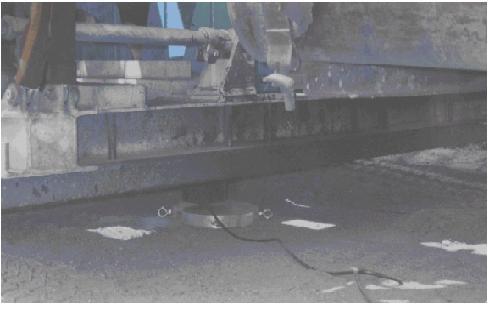 Vibroseis single-point-plate loading system. This image taken from just above pavement level shows the lower portion of the Vibroseis truck with a single-point plate in contact with the pavement. A round steel plate with dimensions of 0.3-meter (1-foot) diameter and 25.4-millimeter (1-inch) thickness is placed between the bridge deck and a Beowulf load cell.