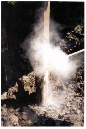 Shearing of pile of bent 12. This image shows a cloud of dust as the south pile/column of bent 12 of the Trinity River Relief Bridge is being sheared and broken by a vibrating breaker point on a backhoe.