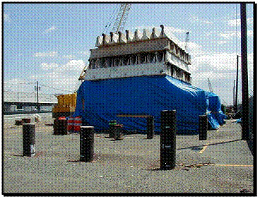 Figure 7. Photo. Port of Elizabeth demonstration site. This figure is a color photograph of the location of the experimental tests conducted to address research and development needs, and to assess the feasibility of using fiber-reinforced polymer composite piles as vertical load-bearing piles. The demonstration site is located at the Port of Elizabeth in New Jersey, a facility provided by the Port Authority of New York and New Jersey. The photograph shows composite piles in the foreground and testing equipment in the background.