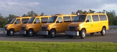 . This figure shows a fleet of four inertial road profilers used to measure International Roughness Index (IRI), ride number (RN), and other roughness indices. Each profiler is a yellow van equipped with the sensors attached to the front bumper. 
