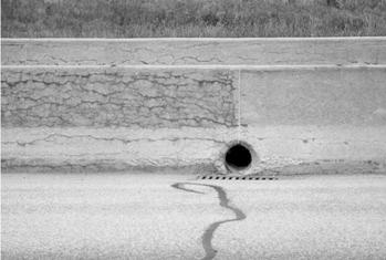 Figure 15. Photo. Barrier wall in Quebec—the section of the wall to the right of the picture has been treated with a silane sealer. This photo shows a concrete wall located next to a pavement. There is a water drain in bottom middle of the wall and a vertical line drawn through the middle of the water drain to near the top of the wall. On the left side of this line, there is extensive map cracking on the wall. On the right side of the wall, cracking is minimal; this section has been treated with a silane sealer.