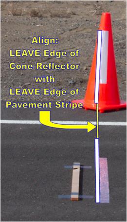 Figure 84. Photo. Placement of vertical photocell target in relation to section starting location. This figure is a photograph that shows the reflective stripe placed at the start of the section and the wood strip that is placed in front of the reflective tape. A cone is placed on the shoulder of the pavement. The leave edge of the reflector on the cone is in line with the leave edge of the reflective tape that is placed on the pavement surface.