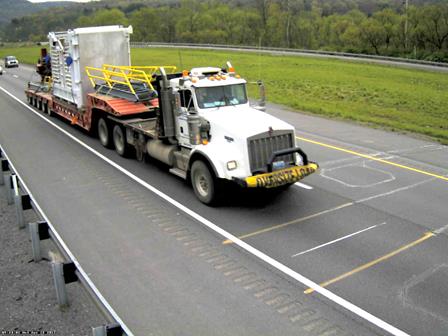 Figure 28. Photo. Image 1 of eight-axle Class 10 truck at Pennsylvania site. This photo shows an eight-axle Class 10 truck consisting of a tractor with a single axle and a tandem axle pulling a five-axle low-boy trailer with an oversize load traveling in the right lane on a highway. 
