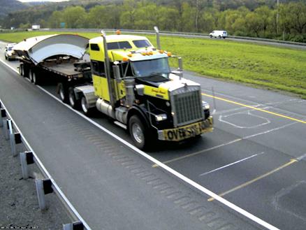 Figure 29. Photo. Image 2 of eight-axle Class 10 truck at Pennsylvania site. This photo shows another eight-axle Class 10 truck consisting of a tractor with a single steering axle and a tridem axle pulling a four-axle (two-tandem) low-boy trailer with an oversize load traveling in the right lane on a highway. 
