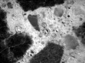  Figure 3-23 (b):  Photographs.  Stereo optical micrographs showing sulfate materials filling air voids.  This figure is comprised of two micrographs, both of which were stained with barium chloride/potassium permanganate to make sulfate materials in the aggregate more visible.  In both micrographs, at least three filled air voids can be seen.