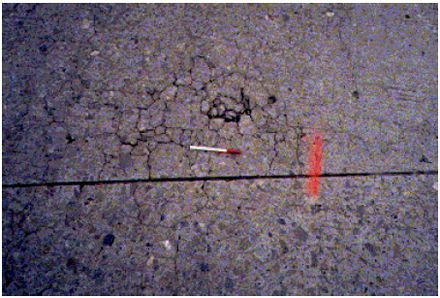 This photograph shows high severity distress in two slabs of concrete. There are large cracks and multiple popouts throughout the slabs.