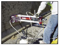 Figure 8. Photo. Core Extraction from a Concrete Barrier along State Highway 2 near Leominster, Massachusetts. This photo shows a contractor operating coring equipment. He is extracting a core (vertically) from a concrete barrier showing ASR damage.