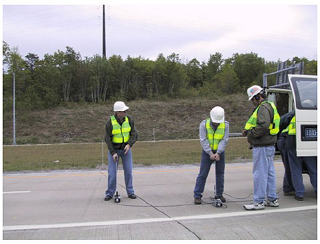 Figure 23.  Photo. Impact Echo Testing-Lackawanna Valley Industrial Highway Experimental Pavement. The photo shows two workers monitoring devices placed on the pavement.