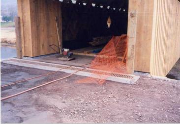 A trench drain before the bridge deck is a solution to fix poor drainage. The picture shows the construction of a trench drain at the bridge's entrance. This system with metal grating in the roadbed prevents the water from entering the bridge.