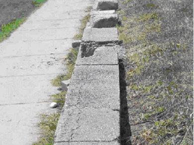 Figure 17. Photo. Deterioration of SRW blocks due to exposure to fertilizers from adjacent golf course. Picture shows three SRW blocks with significant scaling of blocks from grassy area above wall.