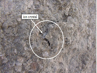 Figure 47. Photo. Breaking off of split face delamination due to ice "jacking" action in field SRW units. The picture shows an arrow pointing to an ice crystal in a crack on the unit.