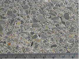Figure 7. Photos. Comparison of internal structures between SRW and ordinary concretes. Photo A shows SRW mix (note compaction voids). Picture shows block of concrete measuring approximately 8 and one half inches on ruler placed at bottom of picture with small deep holes around aggregate throughout surface.