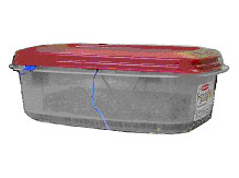 Figure 95. Photo. View of typical specimen in test set a in cabinet freezer in walk-in freezer (N C M A study). Photo of a plastic container with a red lid, showing thermocouple wire leading into the container.
