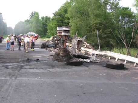 Figure 1. Photo. Remains of tanker truck after fire. This photo shows the remains of the overturned gasoline tanker truck sitting on the bridge deck. The majority of the tanker portion of the truck is missing, having been melted and possibly vaporized by the intense fire.