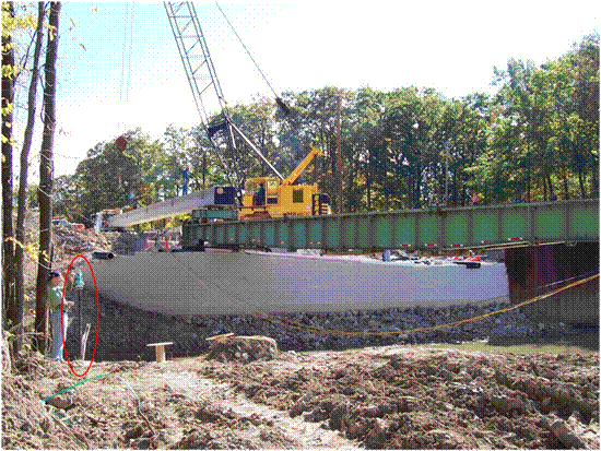 Photo showing the location of a total station reference pole away from a geosynthetic reinforced soil (GRS) abutment being constructed.
