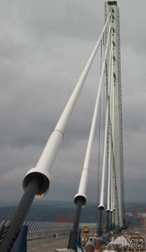 This photo shows modern stay cables with high-density polyethylene (HDPE) tube cover on the Millau Viaduct in France. Cables span from the top right corner to the bottom of the photo, with anchorage guide pipe removed to show the steel strands at the bottom end. The HDPE tube cover is white, and the exposed strands are black.