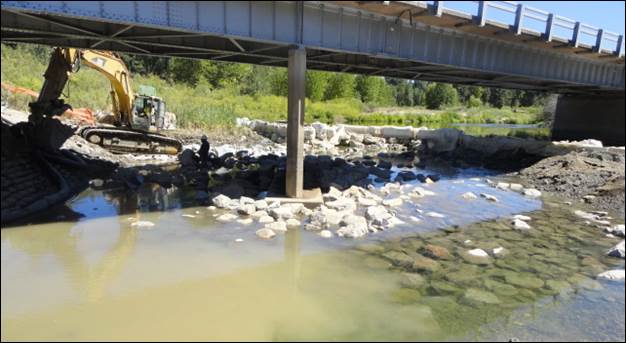 Figure 27. Photo. Riprap installation near pier 3 (August 2012). This photo shows heavy equipment installing the riprap apron at low flow. Many individual rocks appear smaller than was called for in the design.