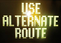 This photograph shows an illuminated dynamic message sign with the words, "Use Alternate Route" on it.