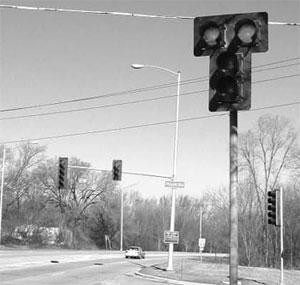 Figure 9. Photo. Photo of signal head using a double red signal indication. The photo shows a signalized intersection with a signal head that has a double-red signal indication on the near side of the intersection. The double-red indications are positioned side-by-side and are centered above the vertical yellow and green indications.