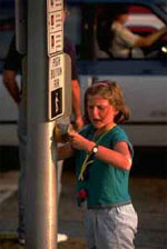 Figure 32. Photo. Pedestrian signals help accommodate pedestrian crossings on some high-volume or multilane roads. The photo shows a young girl pushing a pushbutton for a pedestrian signal.