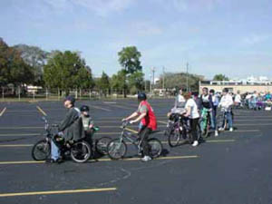 Figure 53: Photo. Many users of various ages and abilities participated in each "Ride for Science." Many participants have just registered and are now lined up across the parking lot, waiting to start. Several appear to be youth.