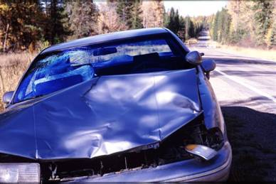 This picture shows a vehicle parked on the side of a two-lane, rural highway. The picture is taken looking at the front end of the vehicle, which has suffered extensive damage.