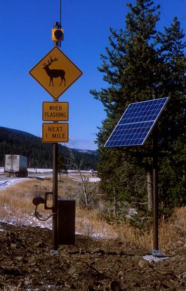  Figure 38. Photo. Animal detection system along Hwy 191 in Yellowstone National Park, Montana. (photo: Marcel Huijser, WTI). This picture shows two posts next to the roadway. The post furthest from the roadway has a solar panel on the top. The post closest to the roadway has a number of items attached to it. From top to bottom this pole has an antenna, a flashing beacon, a yellow diamond sign with a silhouette of an elk, a yellow placard with the words “WHEN FLASHING,” a yellow placard with the words “NEXT 1 MILE,” a microwave transmitter, and a battery/controller cabinet.