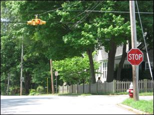 Figure 1. Photo. Example of Standard Overhead Flashing Beacon. Picture of a flashing beacon at a four-way intersection. There is also a STOP sign at the intersection.