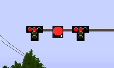 This is a screen capture from the driving simulation. It shows a traffic signal mast arm with a square sign placed equidistant between two traffic signal head assemblies. The traffic signal head assemblies have five lenses arranged in a T. Three red lenses are across the top of the T, and amber and green lenses, respectively, are below the center red lens. In the figure, only the center and left lenses are illuminated. The sign between the two signal head assemblies has a red octagon in the middle and a white strobe light illuminated in the lower right corner of the sign.