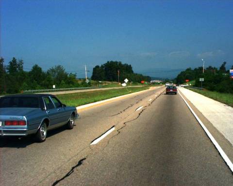Figure 33.  Photograph.  SR-34.  The photograph shows the divided highway on State Route (SR)-34 near Tusculum, TN, along which one of the pavement marking test decks was installed.  Each direction of travel has two lanes.  The photograph is taken from the driver’s perspective from the right lane.  There is a yellow edge line on the left of the two lanes and a white edge line on the right of the two lanes.  Also, there are white dashed lines separating the two lanes.  There is a car in the right lane ahead of the observer’s vehicle, and a car in the left lane that has just passed the observer’s vehicle.  The lanes in the opposing direction can be seen on the left, separated by a grassy median.